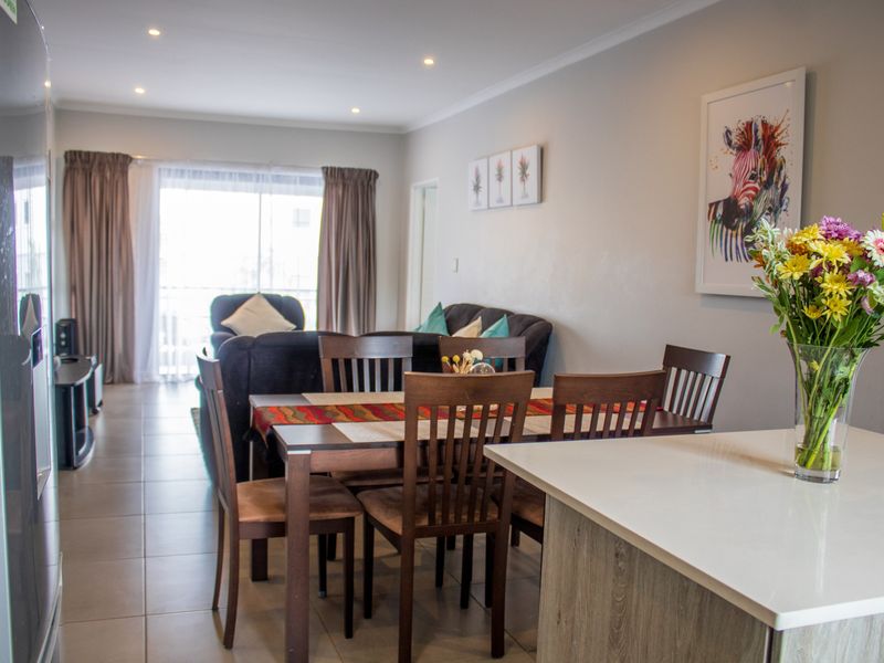 An open-plan living and dining area featuring tiled flooring, recessed lighting, and a kitchen island, leading to a balcony through sliding glass doors.