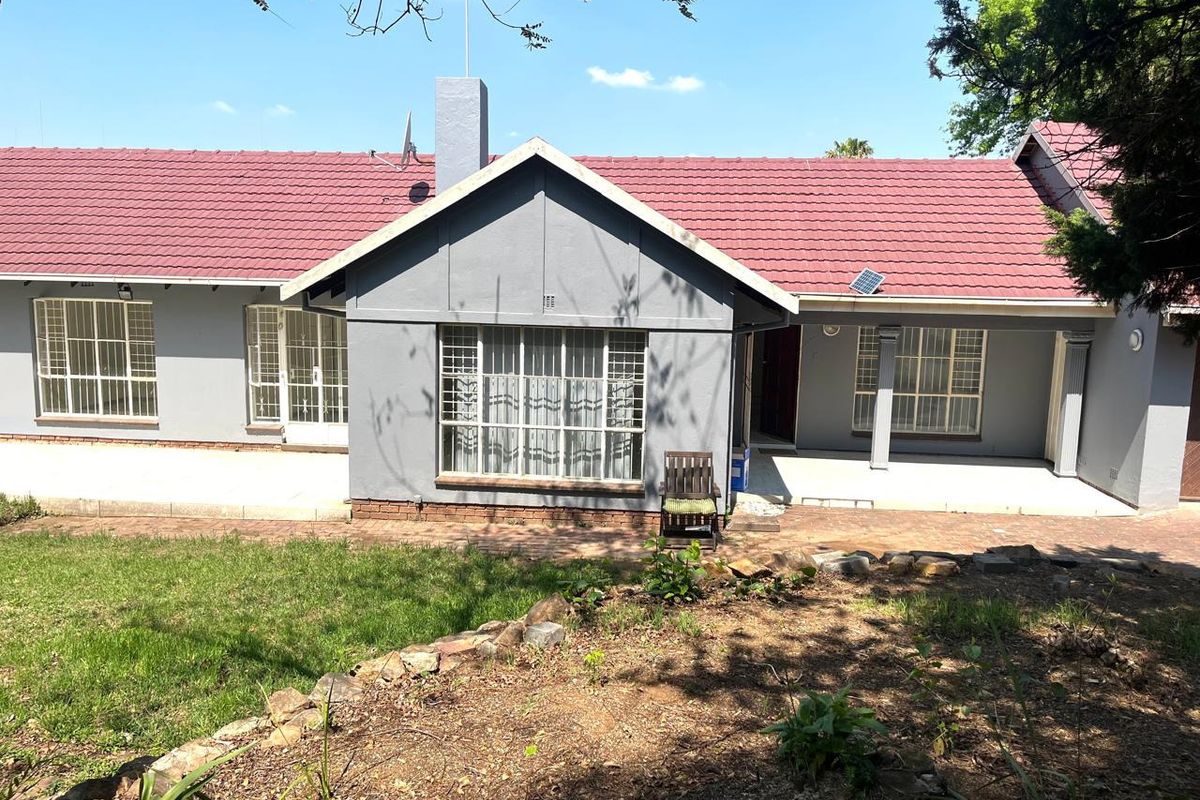 Rear view of the residence featuring a tiled roof, paved patio area, and established garden with a stone retaining wall.