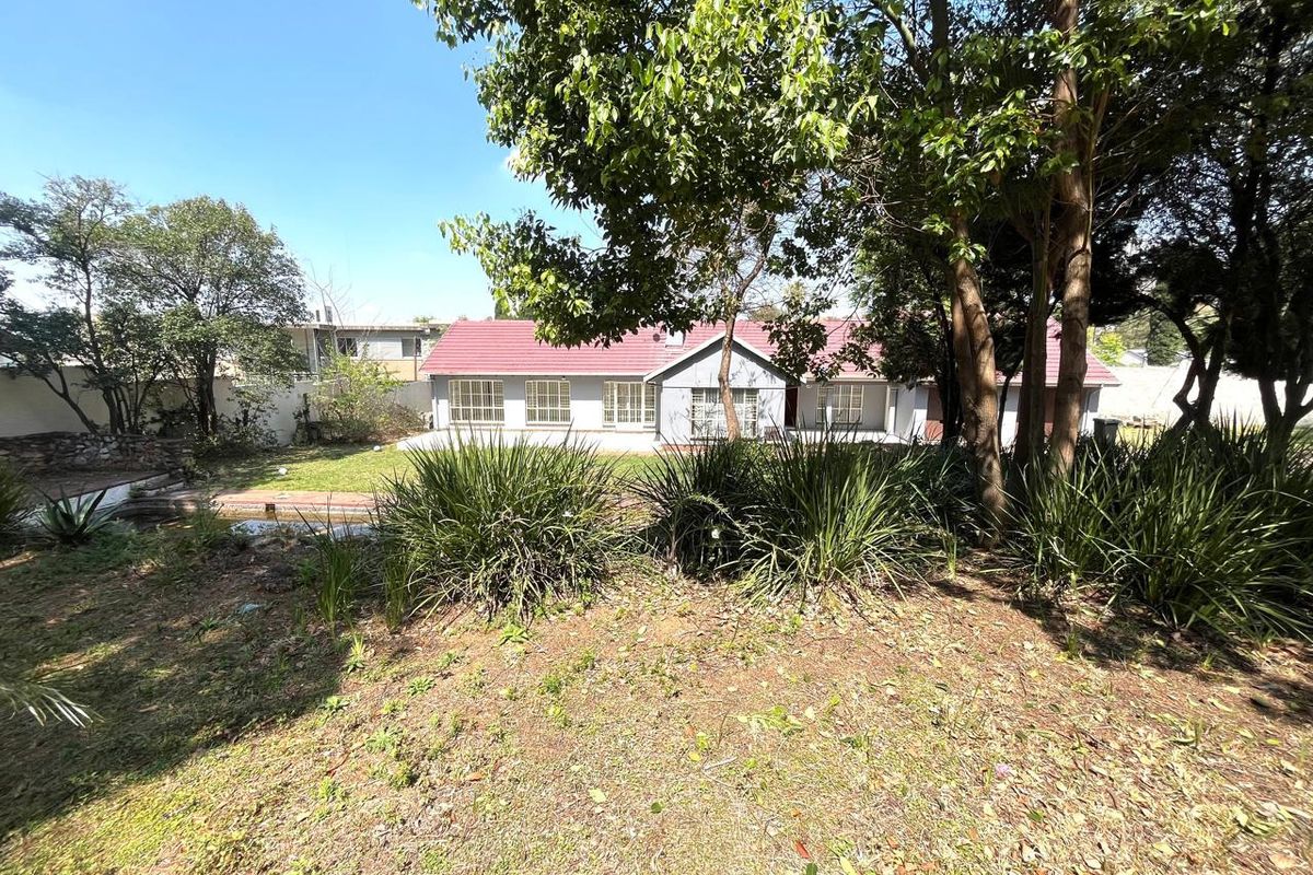 A view of the rear exterior of the residential property featuring a tiled roof, security bars on windows, and a large, mature garden.
