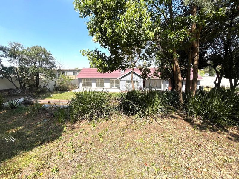 A view of the rear exterior of the residential property featuring a tiled roof, security bars on windows, and a large, mature garden.