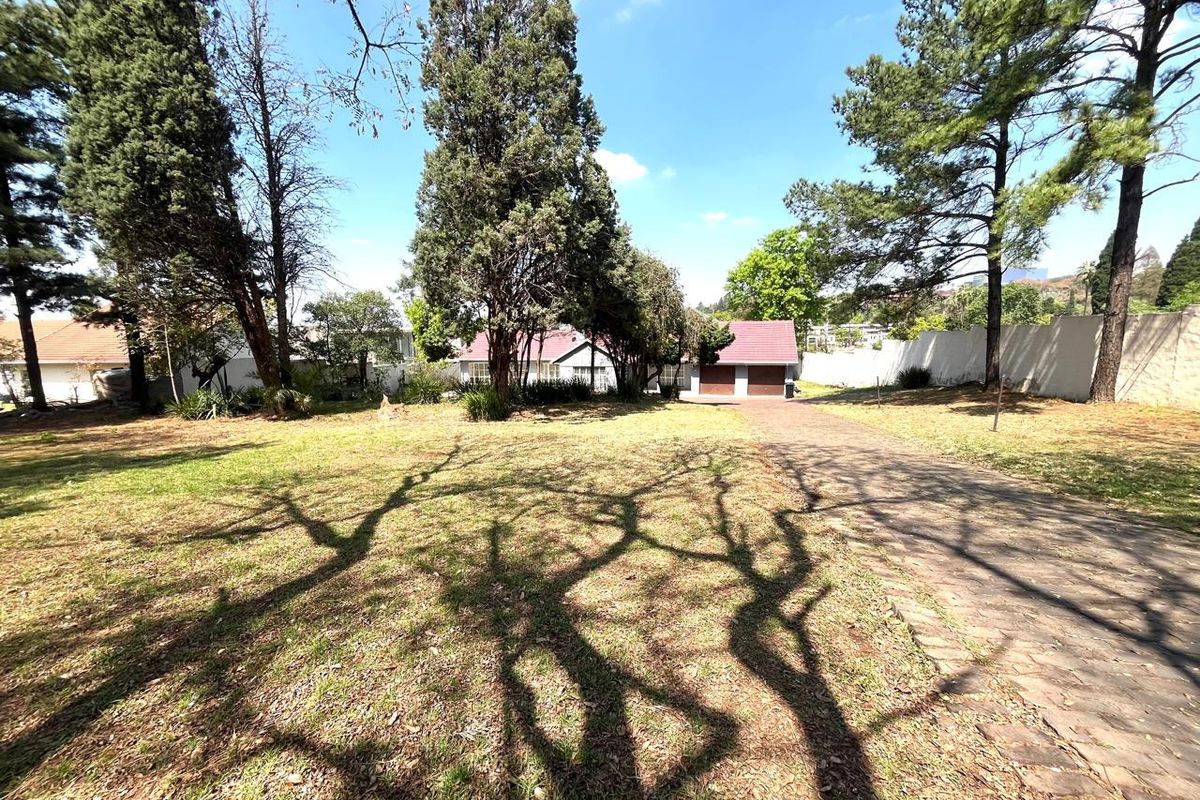 A view of the front yard featuring a paved driveway, mature trees, and a double garage entrance on a residential property.