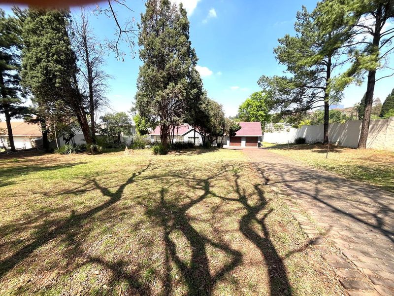 A view of the front yard featuring a paved driveway, mature trees, and a double garage entrance on a residential property.