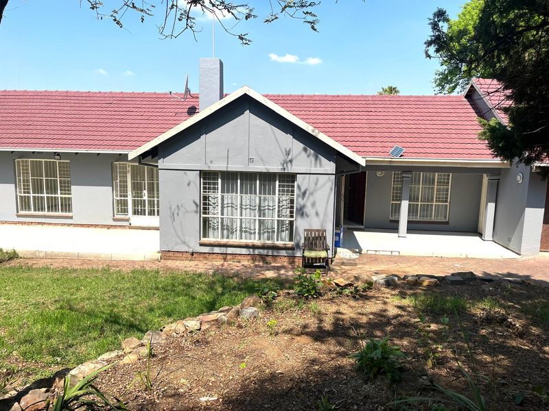 Rear view of the residence featuring a tiled roof, paved patio area, and established garden with a stone retaining wall.