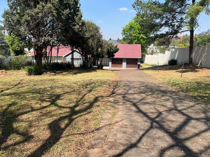 Front view of a residential property featuring a long paved driveway, double garage, and established garden with mature trees.