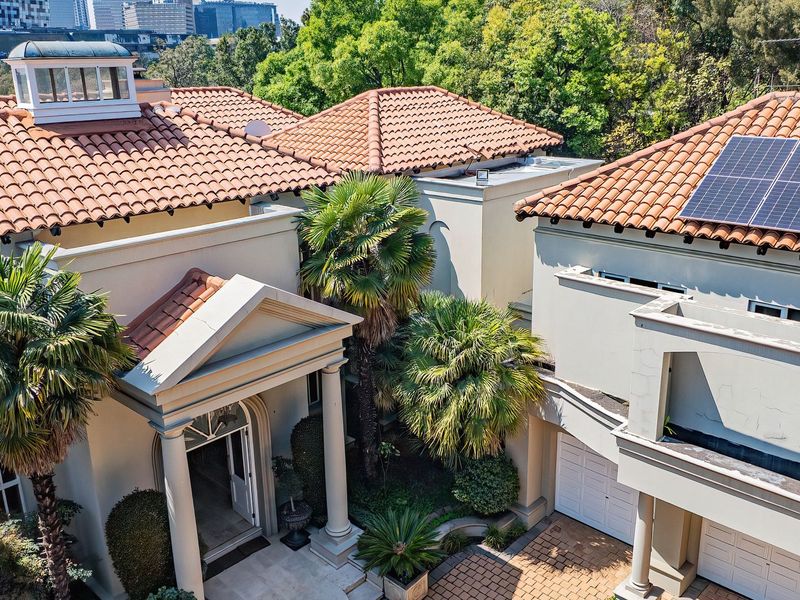 Aerial view of a cluster home featuring a terracotta tiled roof, solar panels, a classic portico entrance, and a paved driveway with double garage.