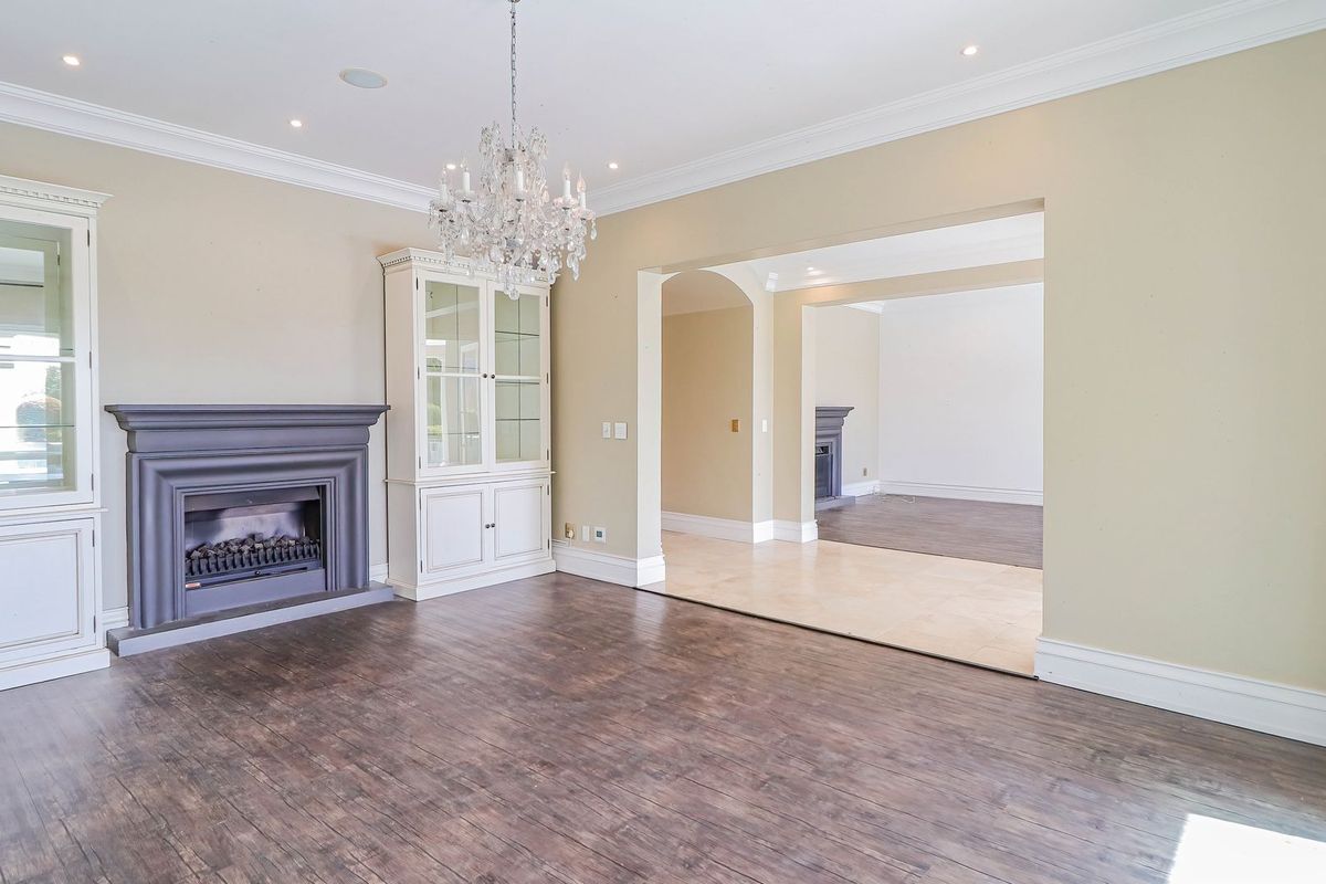 Spacious living room featuring dark laminate flooring, a classic fireplace with built-in cabinetry, elegant crown molding, and an open-plan flow to an adjacent room.