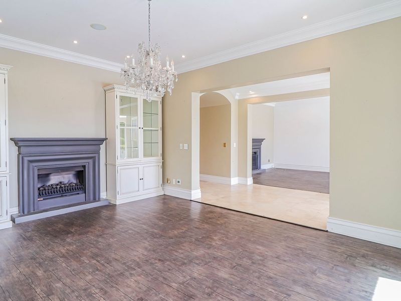Spacious living room featuring dark laminate flooring, a classic fireplace with built-in cabinetry, elegant crown molding, and an open-plan flow to an adjacent room.