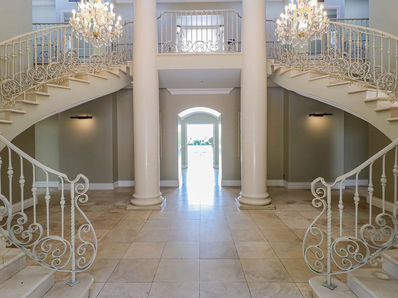 Grand entrance hall featuring a symmetrical dual staircase with ornate wrought iron balustrades, stone flooring, and elegant columns.