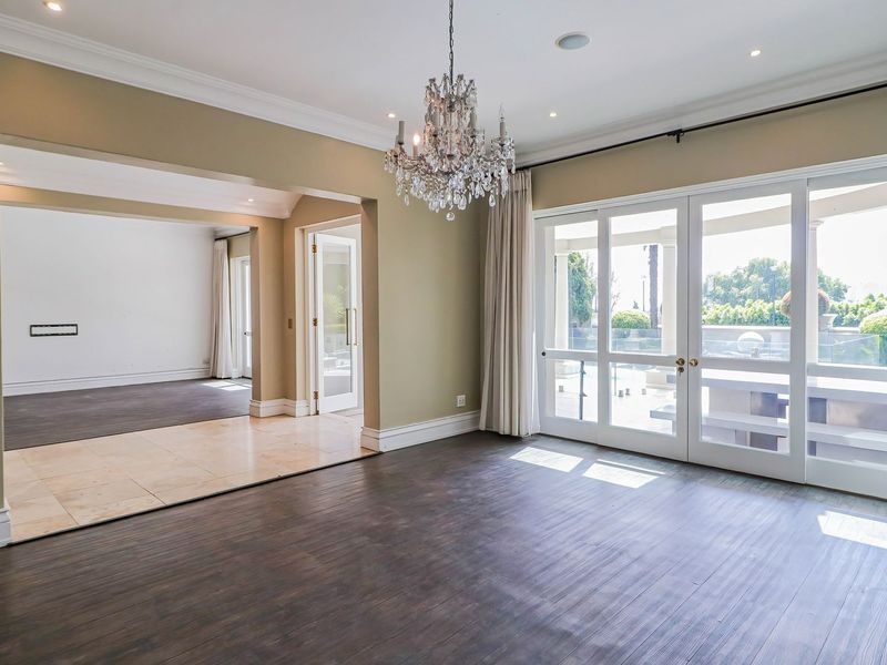 Spacious living area featuring dark laminate flooring, elegant crown molding, a crystal chandelier, and large glass doors opening to an outdoor patio area.
