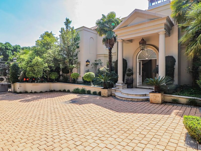 Elegant front entrance featuring a paved driveway, covered portico with columns, and an arched doorway, set within a well-maintained landscaped garden.
