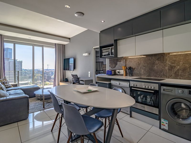 Modern open-plan living area featuring a sleek kitchen with integrated appliances, tiled flooring, and large sliding doors leading to a balcony with city views.