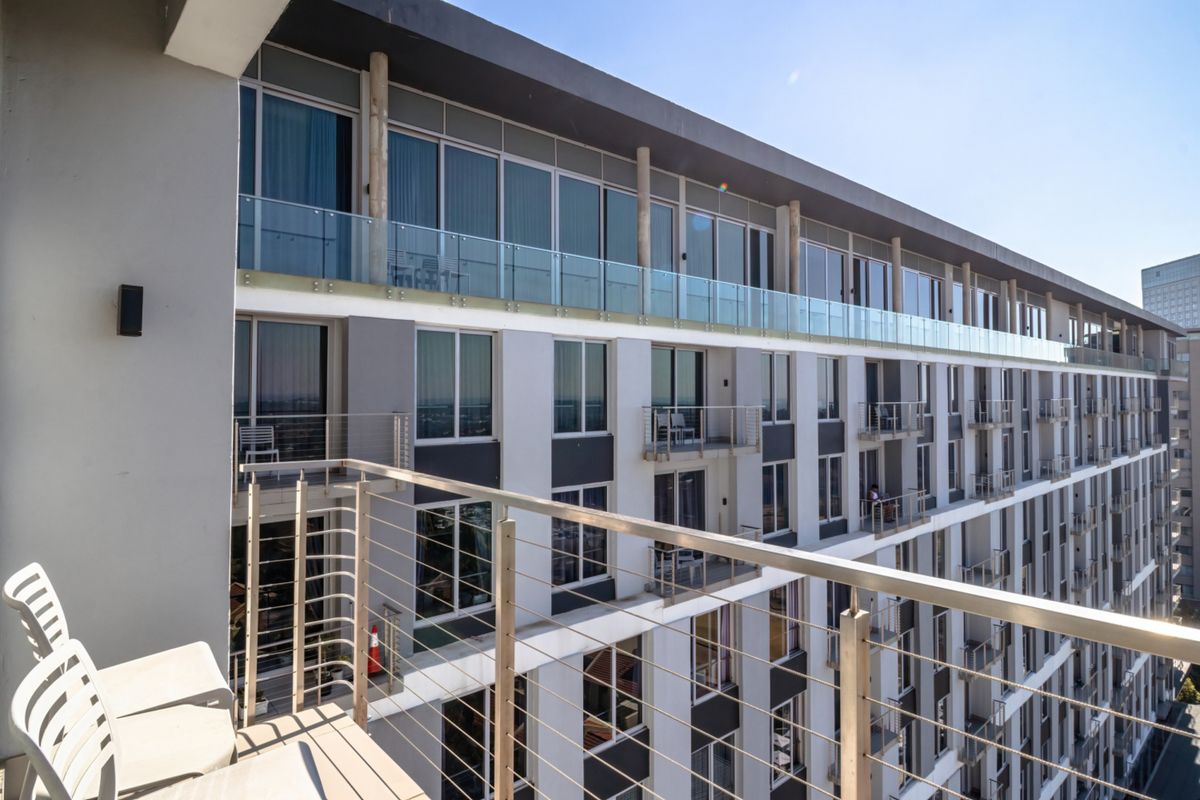 A view of the apartment building exterior featuring multiple levels with glass balustrades and sliding door access to private balconies.