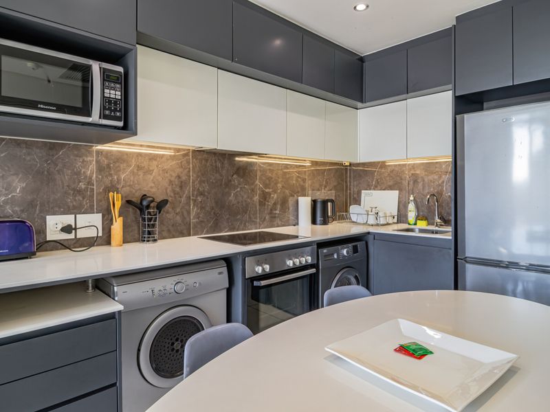 Modern kitchen featuring sleek two-tone cabinetry, stone countertops, marble-look splashback, and integrated appliances including an oven, hob, and microwave.