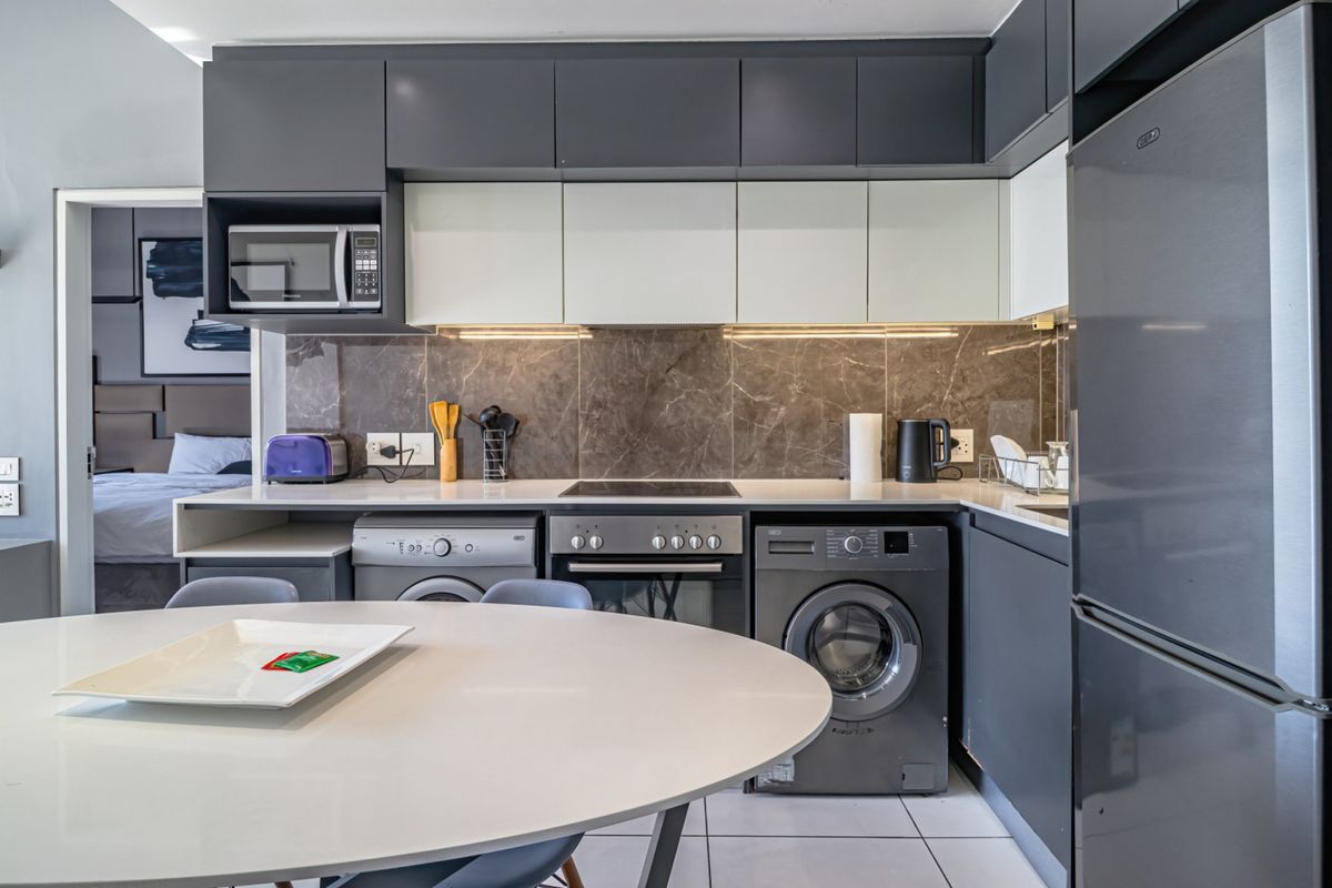 Modern kitchen featuring sleek dark and light cabinetry, stone countertops, marble-look splashback, and integrated appliances, seamlessly connected to the living area.