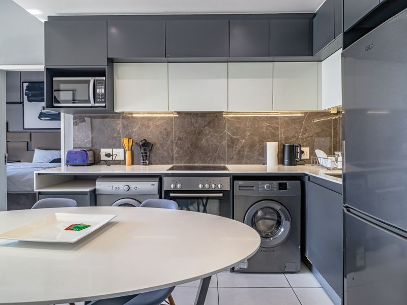 Modern kitchen featuring sleek dark and light cabinetry, stone countertops, marble-look splashback, and integrated appliances, seamlessly connected to the living area.