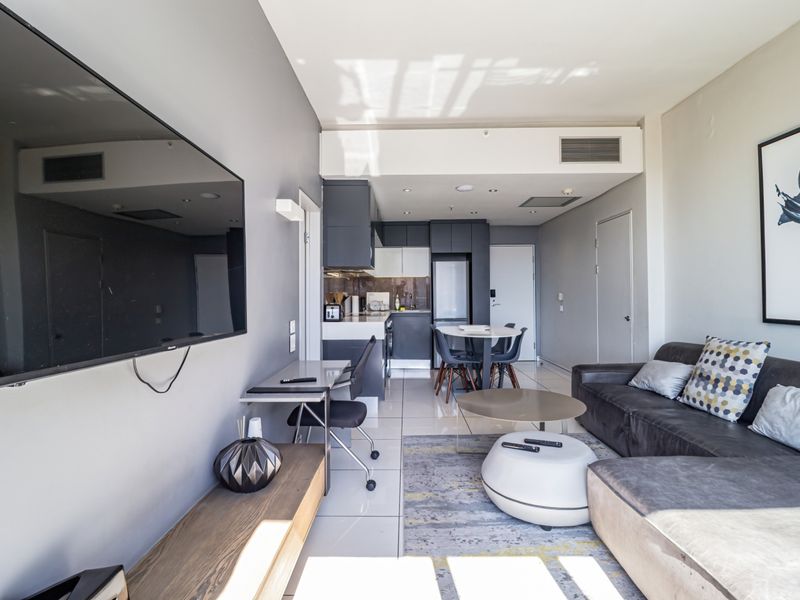 Modern open-plan apartment living area featuring tiled floors, ducted air conditioning, and a compact, well-appointed kitchen with integrated cabinetry.