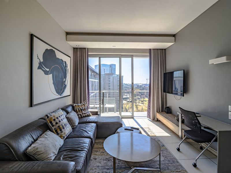 A modern living room featuring tiled floors, recessed lighting, and a large sliding glass door providing access to a balcony with city views.