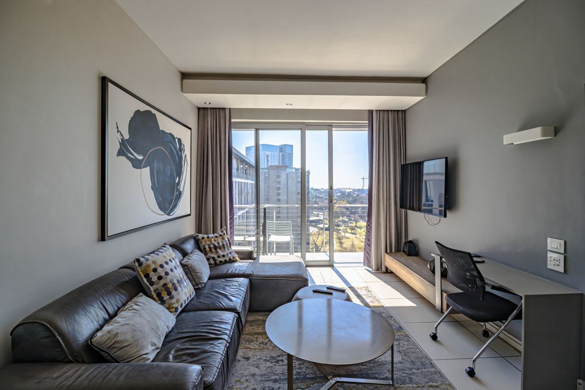 A modern living room featuring tiled floors, recessed lighting, and a large sliding glass door providing access to a balcony with city views.