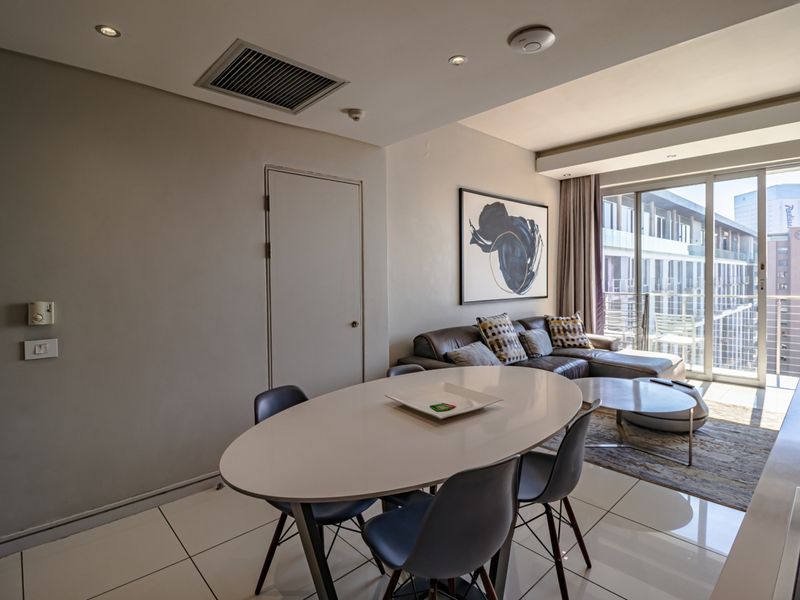 Modern open-plan living and dining area featuring tiled floors, recessed lighting, ducted air conditioning, and large sliding glass doors leading to a balcony.
