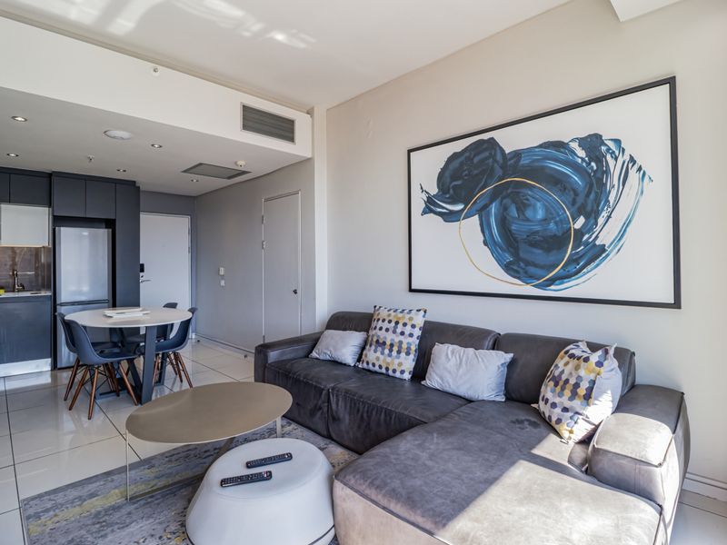 Modern open-plan living area featuring sleek dark cabinetry, tiled flooring, and recessed lighting, seamlessly integrating the kitchen and lounge space.