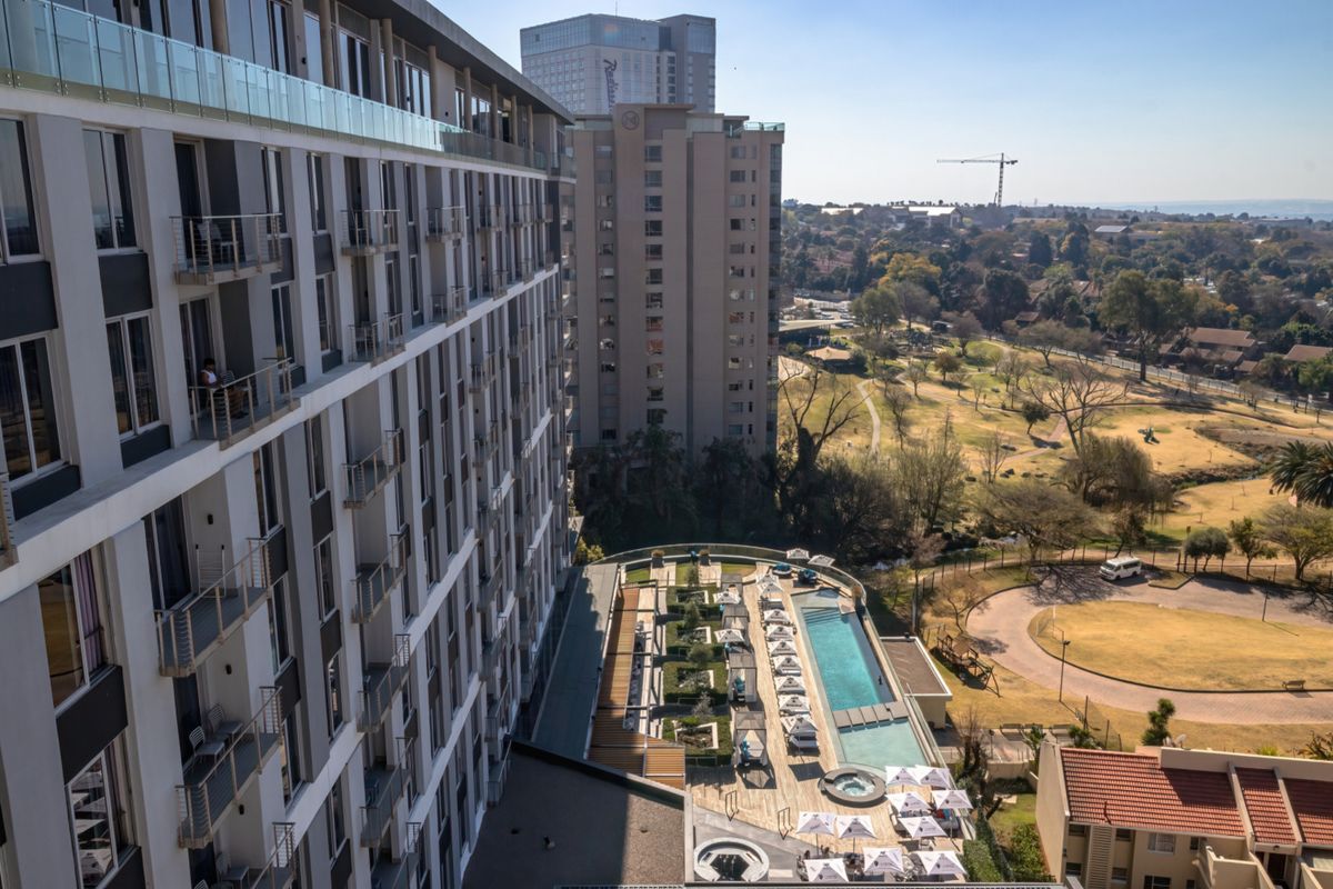 Aerial view of the apartment complex featuring a modern swimming pool, landscaped garden area, and private balconies with glass balustrades.