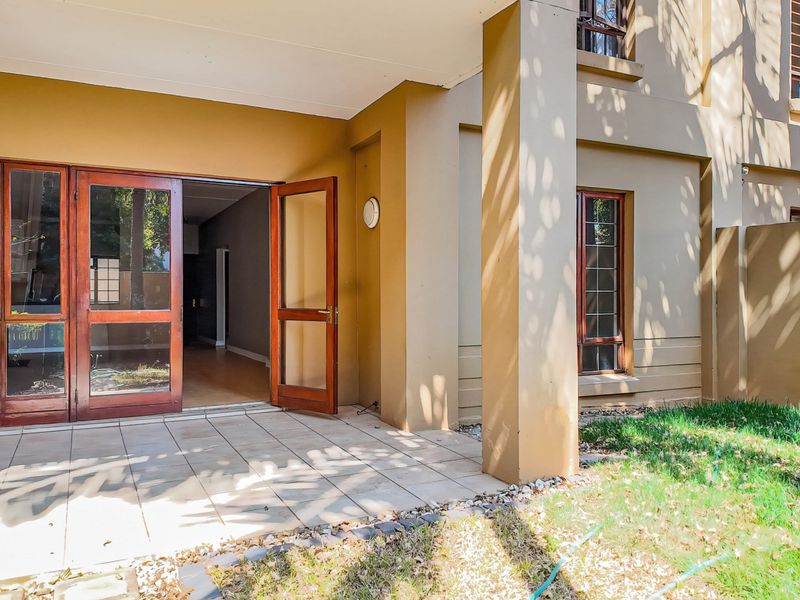 A covered patio area featuring tiled flooring and wooden framed glass doors leading into the interior living space.
