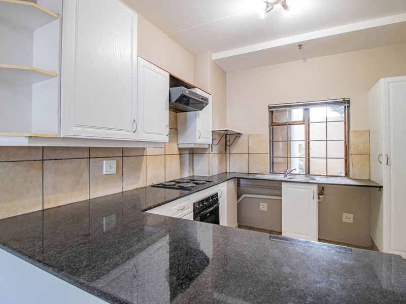 A functional kitchen featuring granite countertops, built-in oven, electric hob, extractor fan, and ample cabinetry with a tiled backsplash.