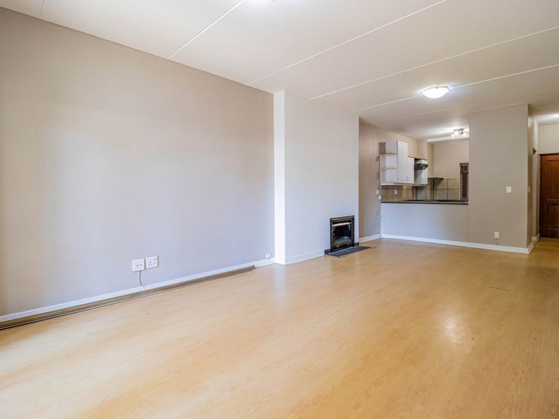Spacious open-plan living area featuring laminate flooring, a built-in fireplace, and a functional kitchen with cabinetry, leading to a separate room entrance.