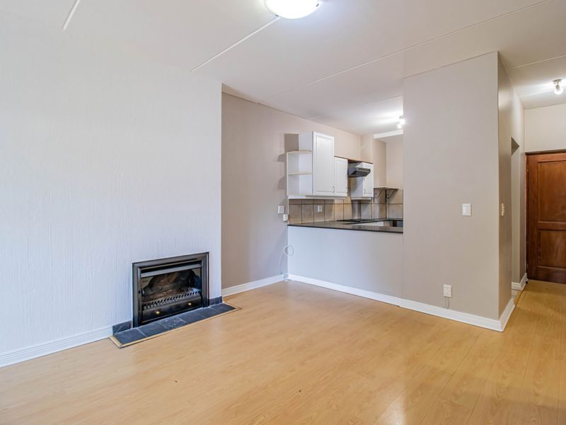 Open-plan living area featuring a built-in fireplace, laminate flooring, and a compact kitchen with cabinetry and tiled backsplash.