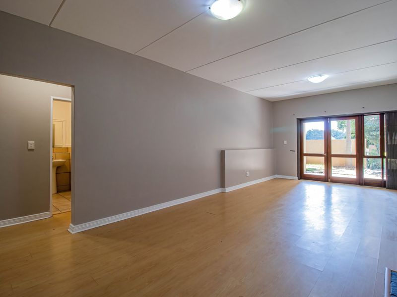 Spacious, empty living area featuring laminate flooring, neutral walls, and double glass doors providing access to the exterior.