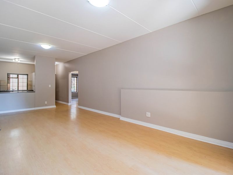 Spacious open-plan living area featuring light laminate flooring, neutral walls, and a functional kitchen space with built-in cabinetry.