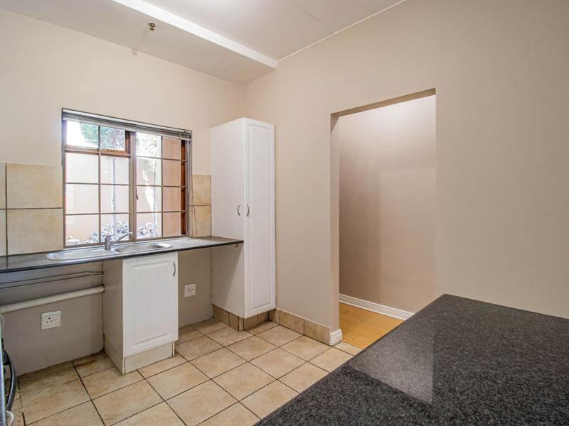 A functional kitchen featuring granite countertops, a stainless steel sink, tiled flooring, and built-in cabinetry, offering a clean space ready for updates.