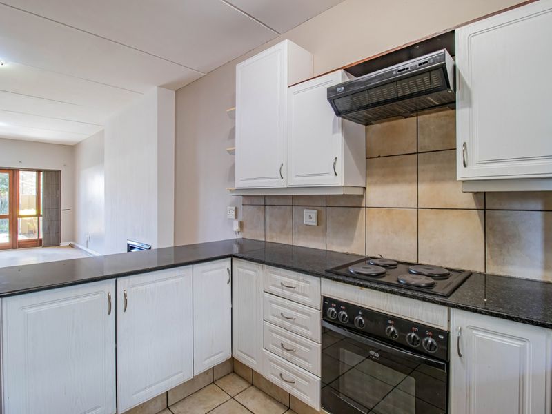 A functional kitchen featuring white cabinetry, granite countertops, a built-in oven, and an electric hob, with an open-plan layout leading to the living area.