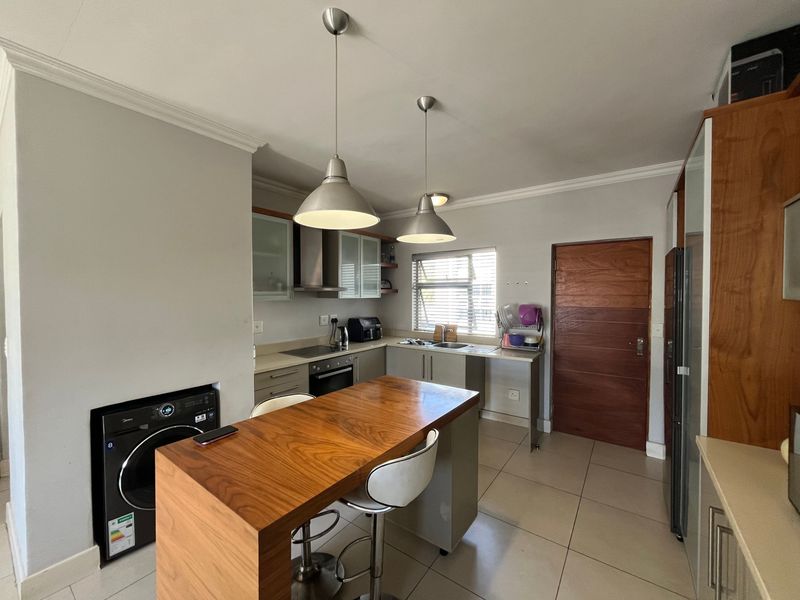 A modern kitchen featuring built-in cabinetry, stone countertops, integrated appliances, and a wooden breakfast bar, complemented by tiled flooring and pendant lighting.