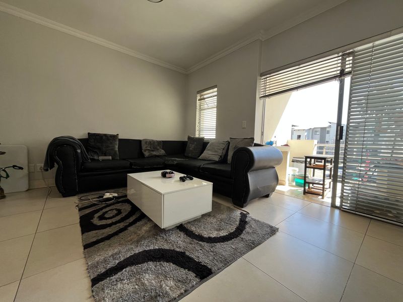 A bright living room featuring tiled flooring and a large sliding glass door providing access to an outdoor balcony area.