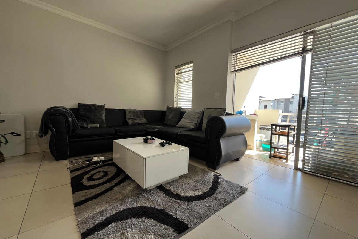 A bright living room featuring tiled flooring and a large sliding glass door providing access to an outdoor balcony area.