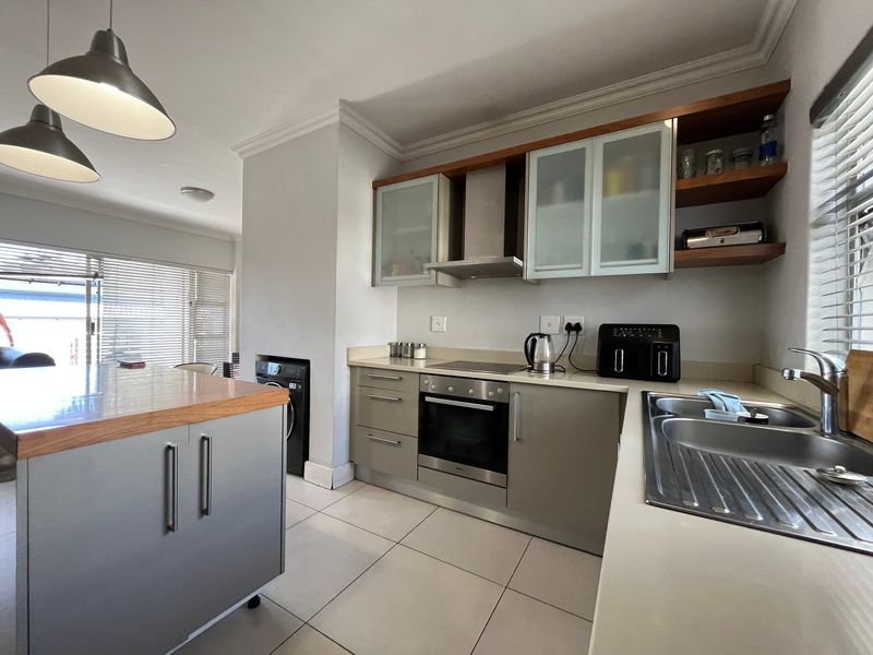 Modern kitchen featuring a central island, built-in oven, electric hob, extractor fan, and stainless steel sink with ample cabinetry and tiled flooring.