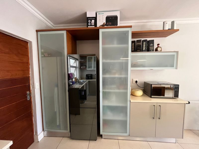 A functional kitchen area featuring built-in cabinetry with frosted glass accents, laminate countertops, and a built-in microwave, set against tiled flooring.