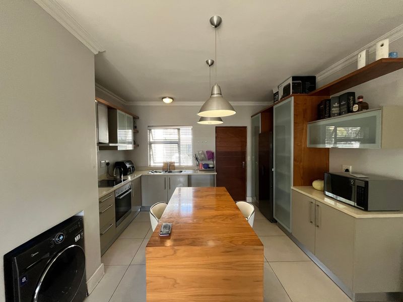 A functional kitchen featuring built-in cabinetry, a central wooden island, stainless steel sink, and integrated appliances with tiled flooring throughout.