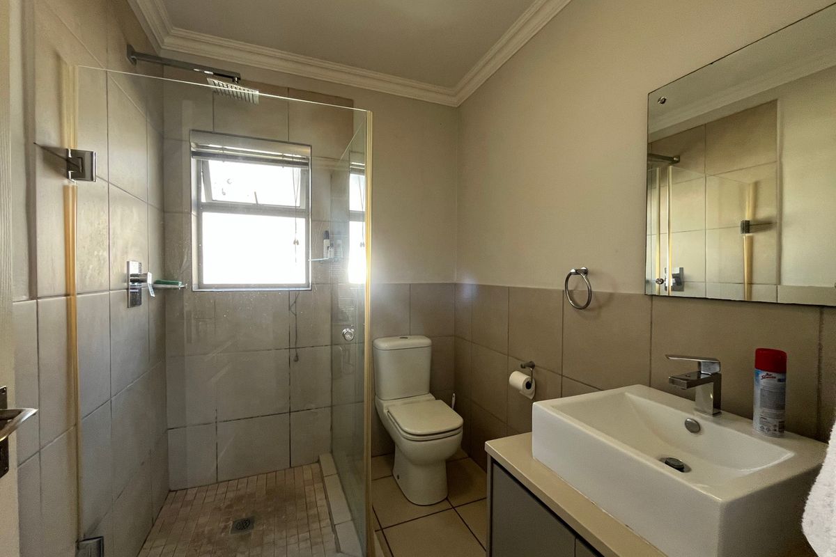 A functional bathroom featuring a glass-enclosed shower, a modern basin with vanity storage, and neutral wall and floor tiling.