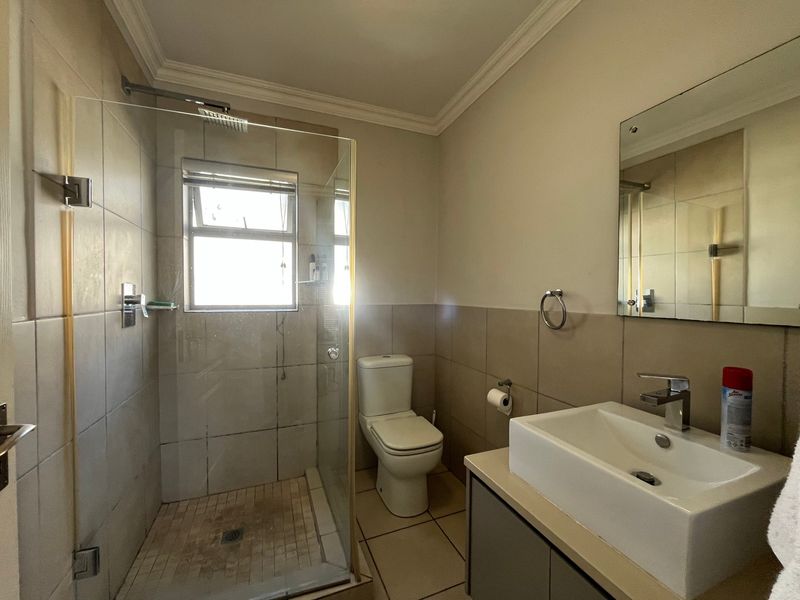 A functional bathroom featuring a glass-enclosed shower, a modern basin with vanity storage, and neutral wall and floor tiling.