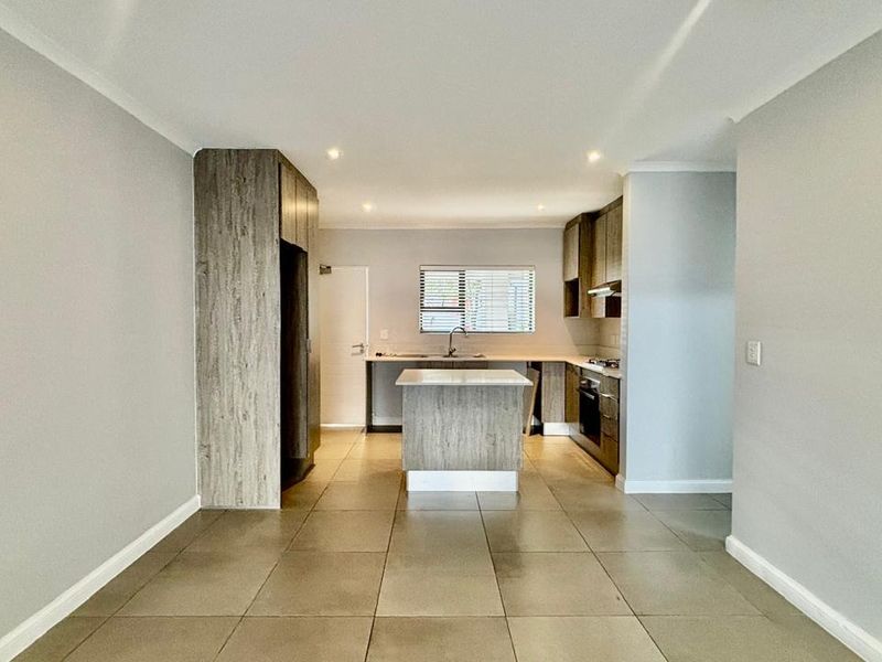 Modern open-plan kitchen featuring built-in cabinetry, a central island, integrated oven and hob, and neutral tiled flooring.