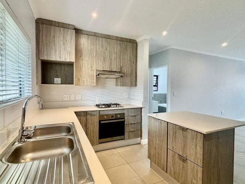 Modern open-plan kitchen featuring wood-grain cabinetry, stone countertops, a kitchen island, and integrated appliances, flowing seamlessly into the adjacent living area.
