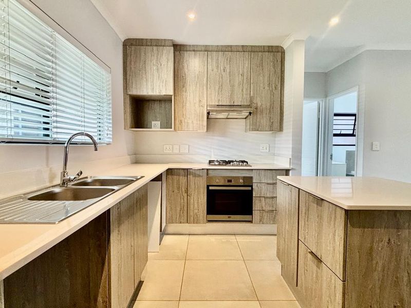 Modern kitchen featuring wood-look cabinetry, stone countertops, a central island, and integrated stainless steel appliances including a gas hob and oven.