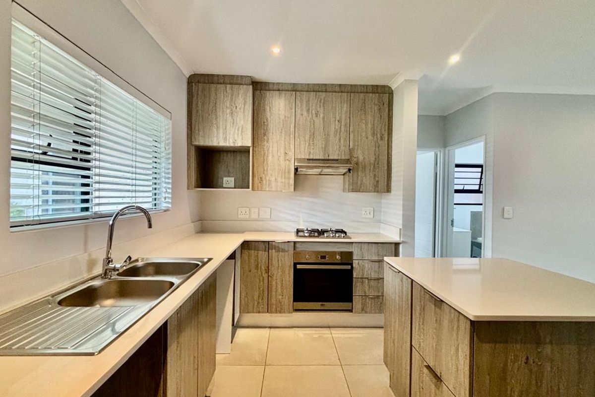 Modern kitchen featuring wood-look cabinetry, stone countertops, a central island, and integrated stainless steel appliances including a gas hob and oven.