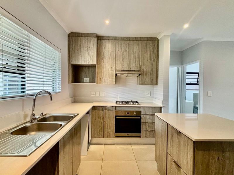 Modern kitchen featuring wood-look cabinetry, stone countertops, a central island, and integrated stainless steel appliances including a gas hob and oven.