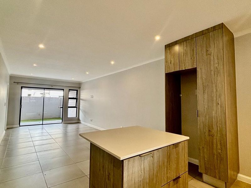Spacious open-plan living area featuring modern tiled flooring, recessed lighting, and a functional kitchen island with built-in cabinetry, leading to an outdoor patio.
