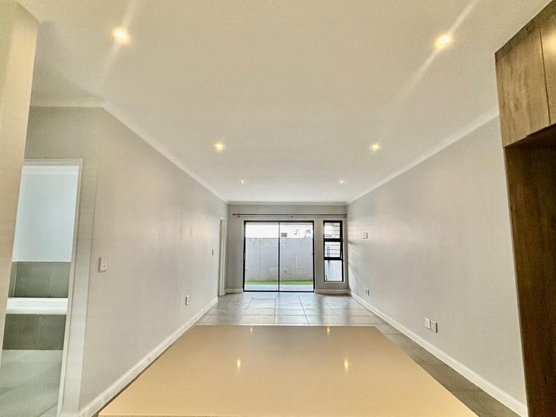 A bright and spacious open-plan living area featuring modern tiled flooring, recessed lighting, and a sliding glass door leading to the exterior.