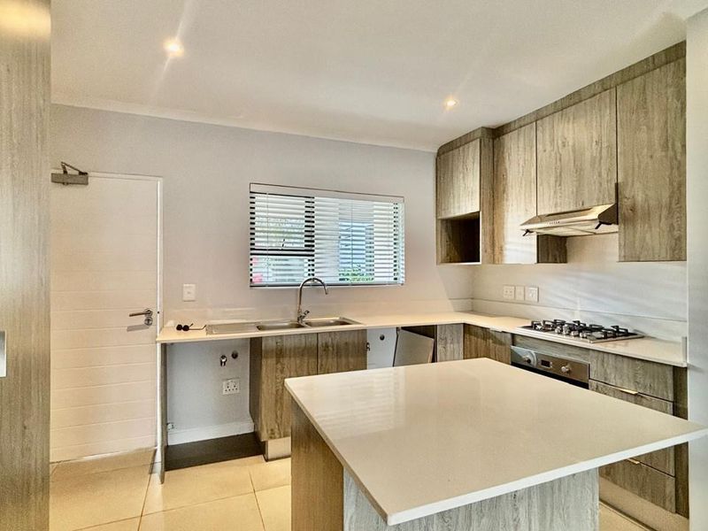 Modern kitchen featuring wood-look cabinetry, stone countertops, a central island, and integrated stainless steel appliances, including a gas hob and oven.