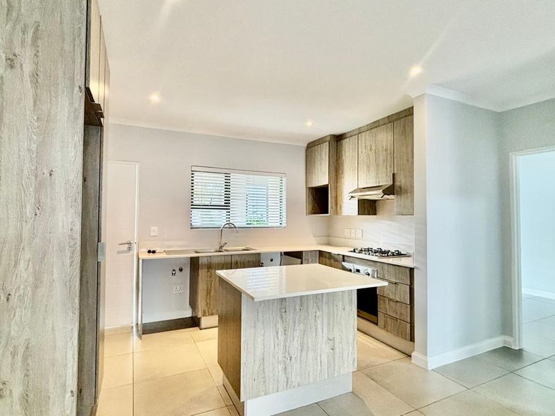 Modern kitchen featuring light wood-grain cabinetry, stone countertops, a central island, and integrated stainless steel appliances with neutral tiled flooring.